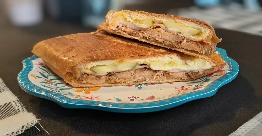 A pressed Cuban sandwich sliced in half, showing layers of pork, ham, swiss and pickles