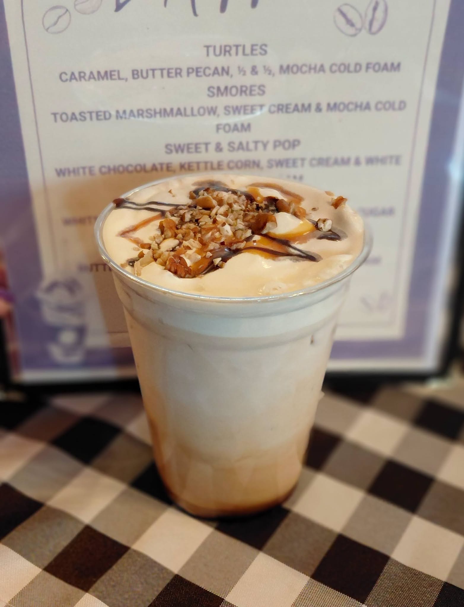 Iced coffee drink topped with whipped cream, pecans and caramel drizzle